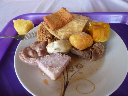 Matoke (a starchy banana), rice, sweet potato, maize porridge (the wedge in front), deep fried potato and white bread, flat bread, ground nut sauce, a little piece of meat, and a pineapple.